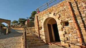 A stone staircase leading to a building with an arched entrance, surrounded by stone walls and vegetation. - Casale del Golfo (Alcamo)