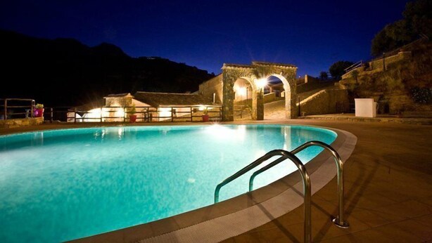 A swimming pool with a stone archway and a metal ladder, surrounded by a stone wall and a hillside. - Casale del Golfo (Alcamo)