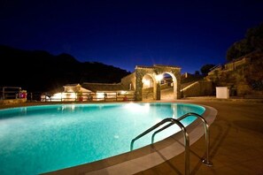 A swimming pool with a stone archway and a metal ladder, surrounded by a stone wall and a hillside. - Casale del Golfo (Alcamo)