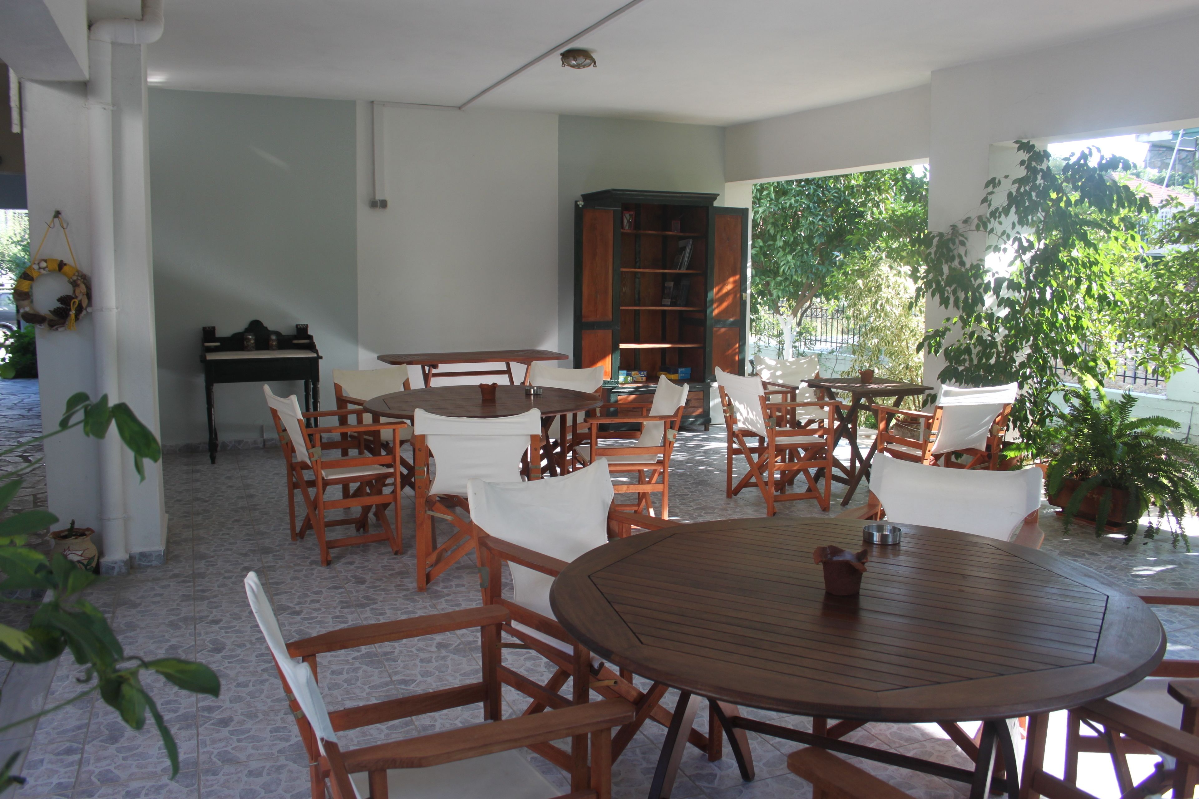 A spacious patio with wooden tables and chairs, a bookshelf, and potted plants.