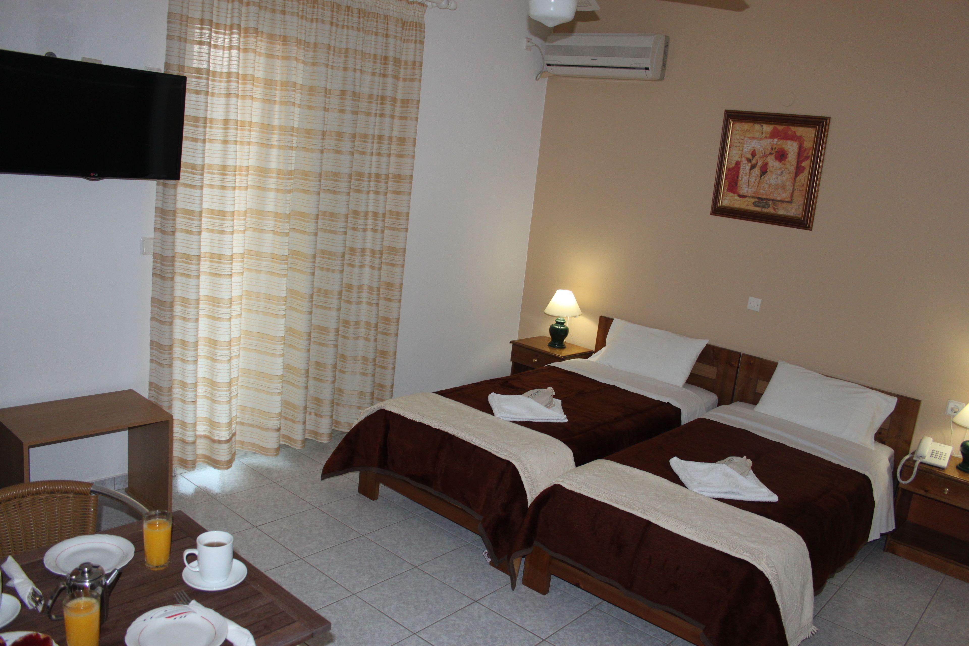 A hotel room with two beds, a television, a painting, a lamp, and a breakfast setup with plates, cups, and juice.
