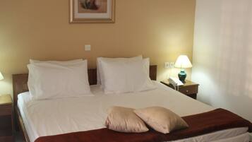 A hotel room with a large bed, a nightstand with a lamp, and a wall-mounted air conditioner.
