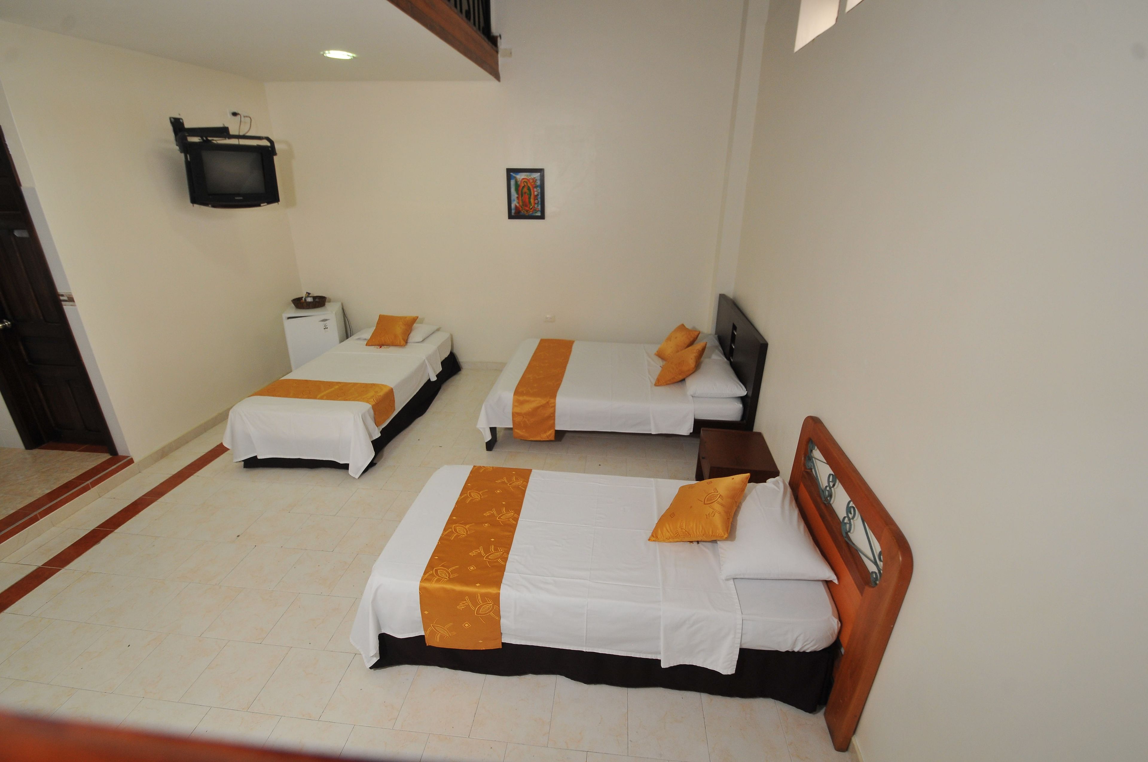 Een hotelkamer met twee bedden, elk voorzien van witte beddengoed en oranje accenten, een klein televisietoestel aan de muur en een ingelijst schilderij boven de bedden.