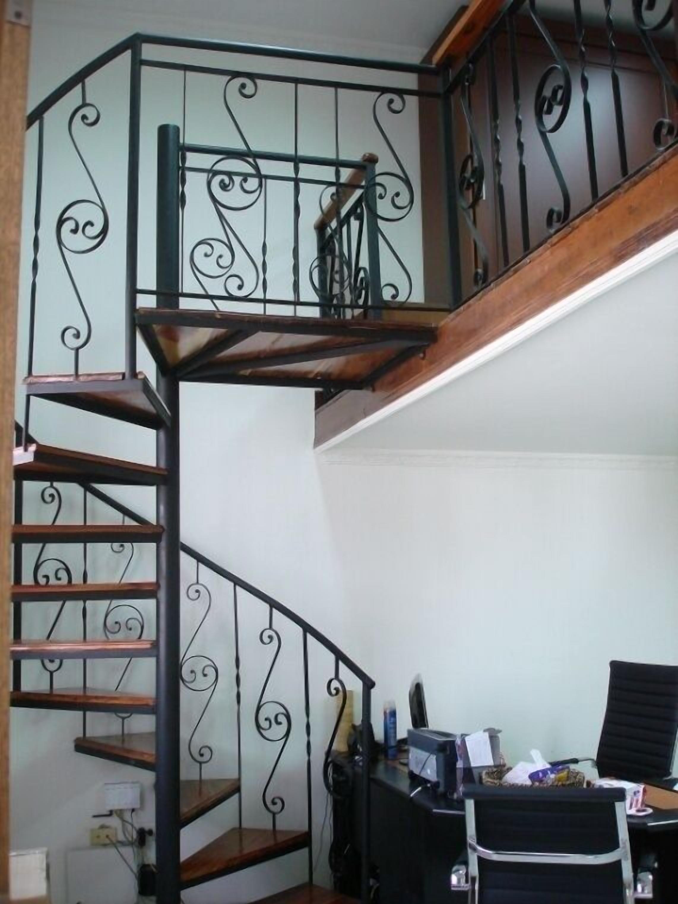 Una escalera de caracol con barandilla metálica y escalones de madera, que conduce a un piso superior.