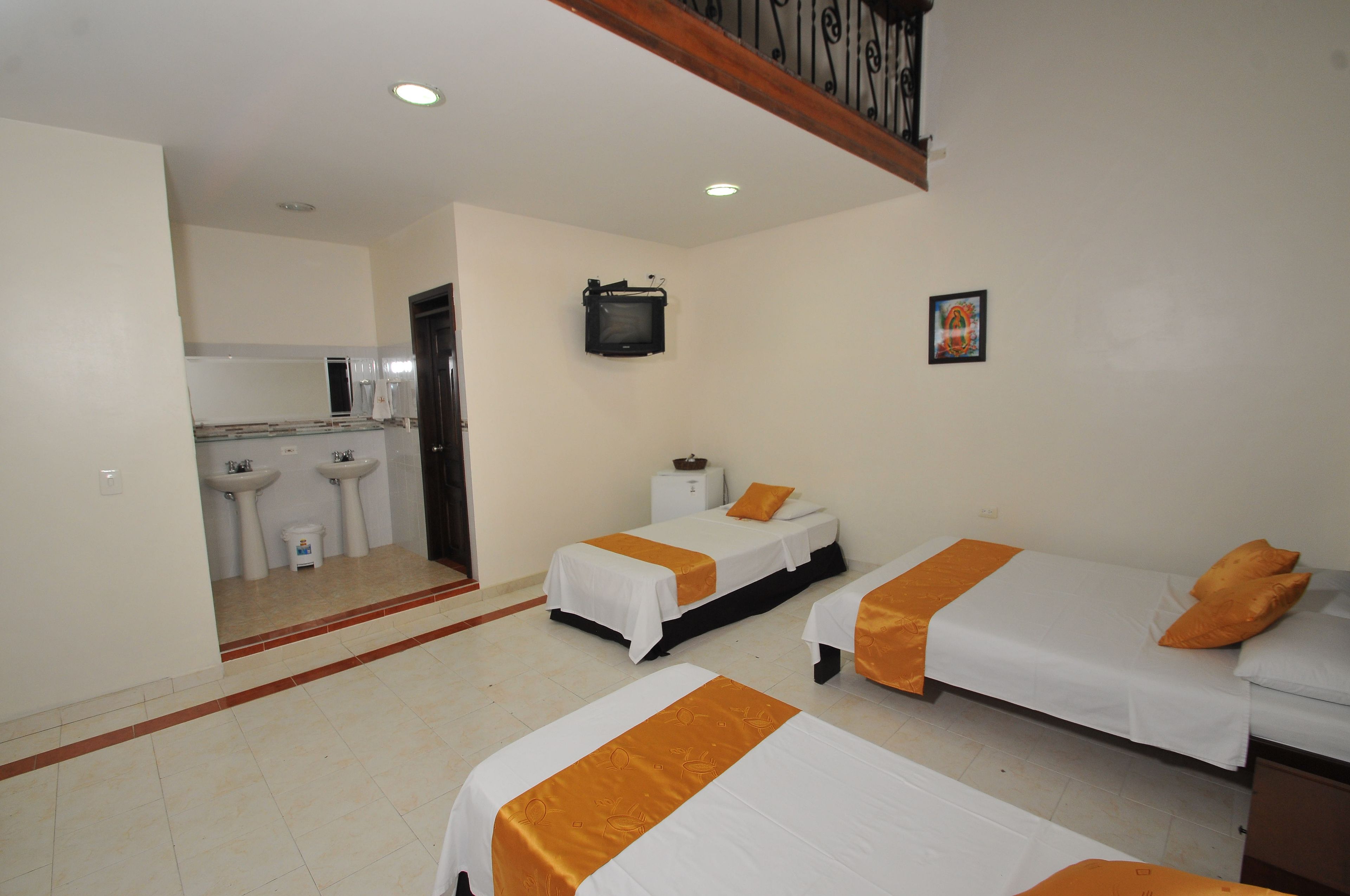 A hotel room with two beds, a television, a small kitchenette, and a bathroom with sinks.