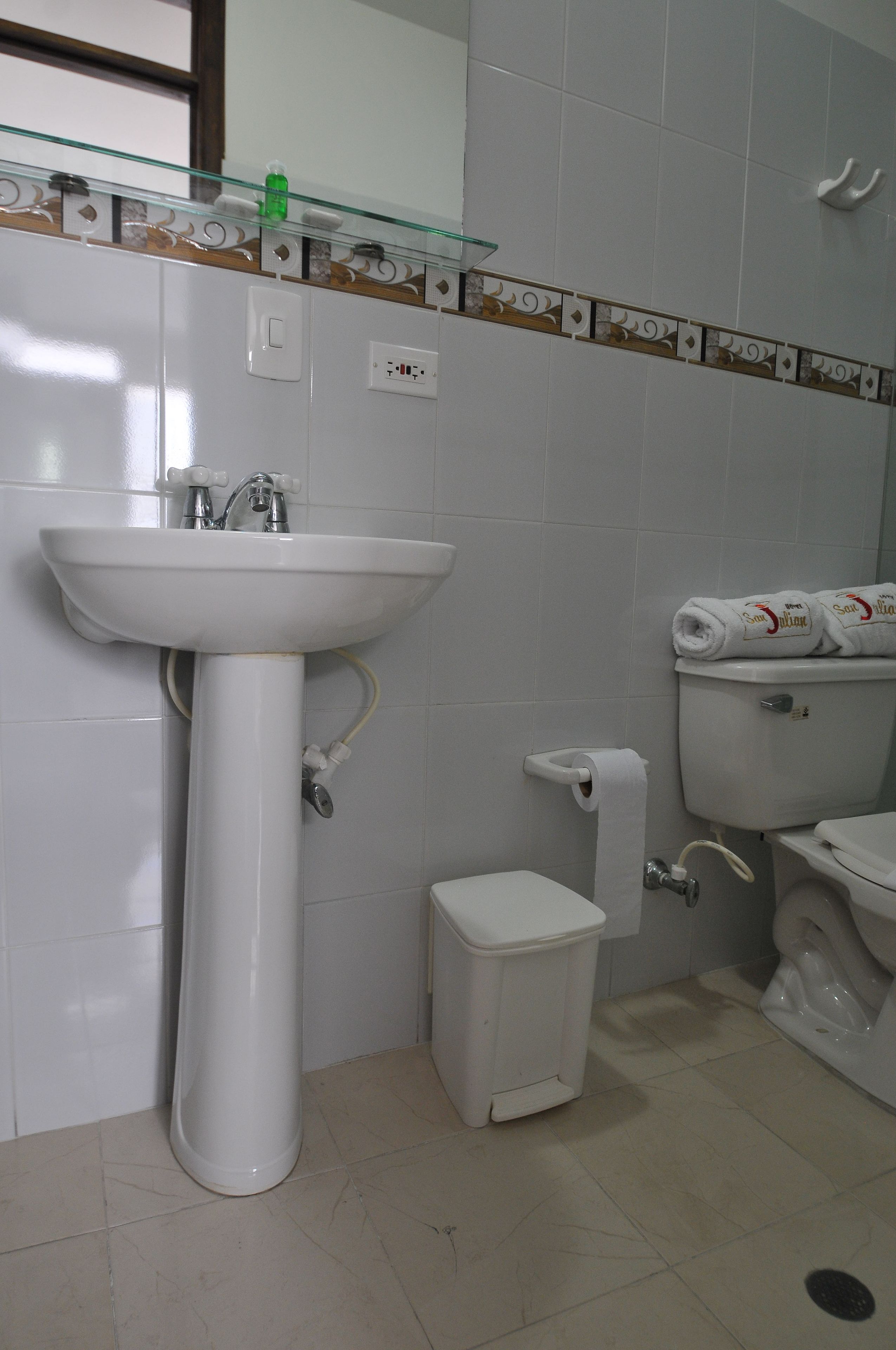 Un baño con lavamanos blanco, inodoro y cubo de basura.