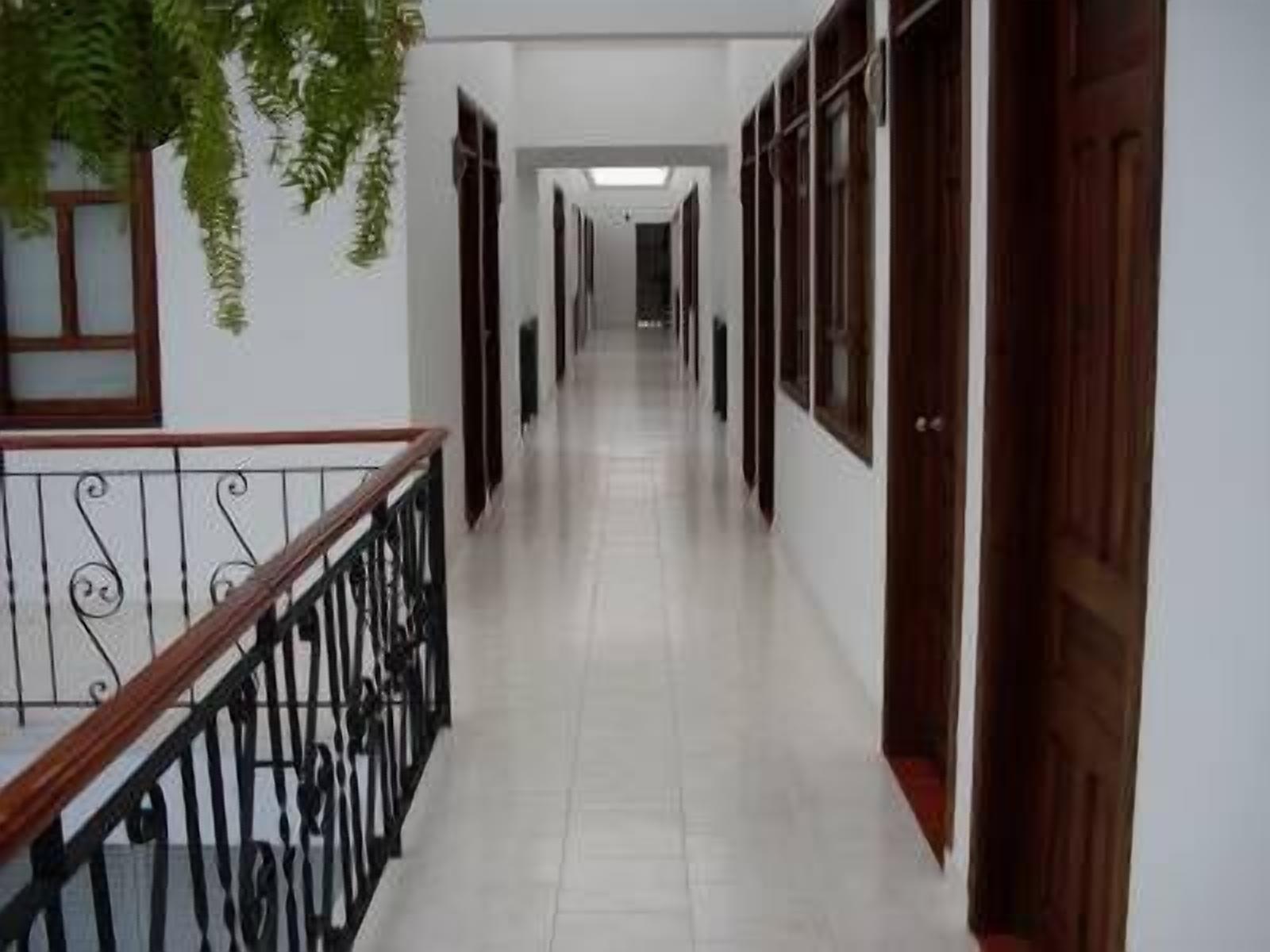 A corridor with a tiled floor, wooden doors, and a metal railing on one side.