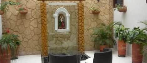 A lobby with a stone wall, a glass enclosure with a statue, and several potted plants.
