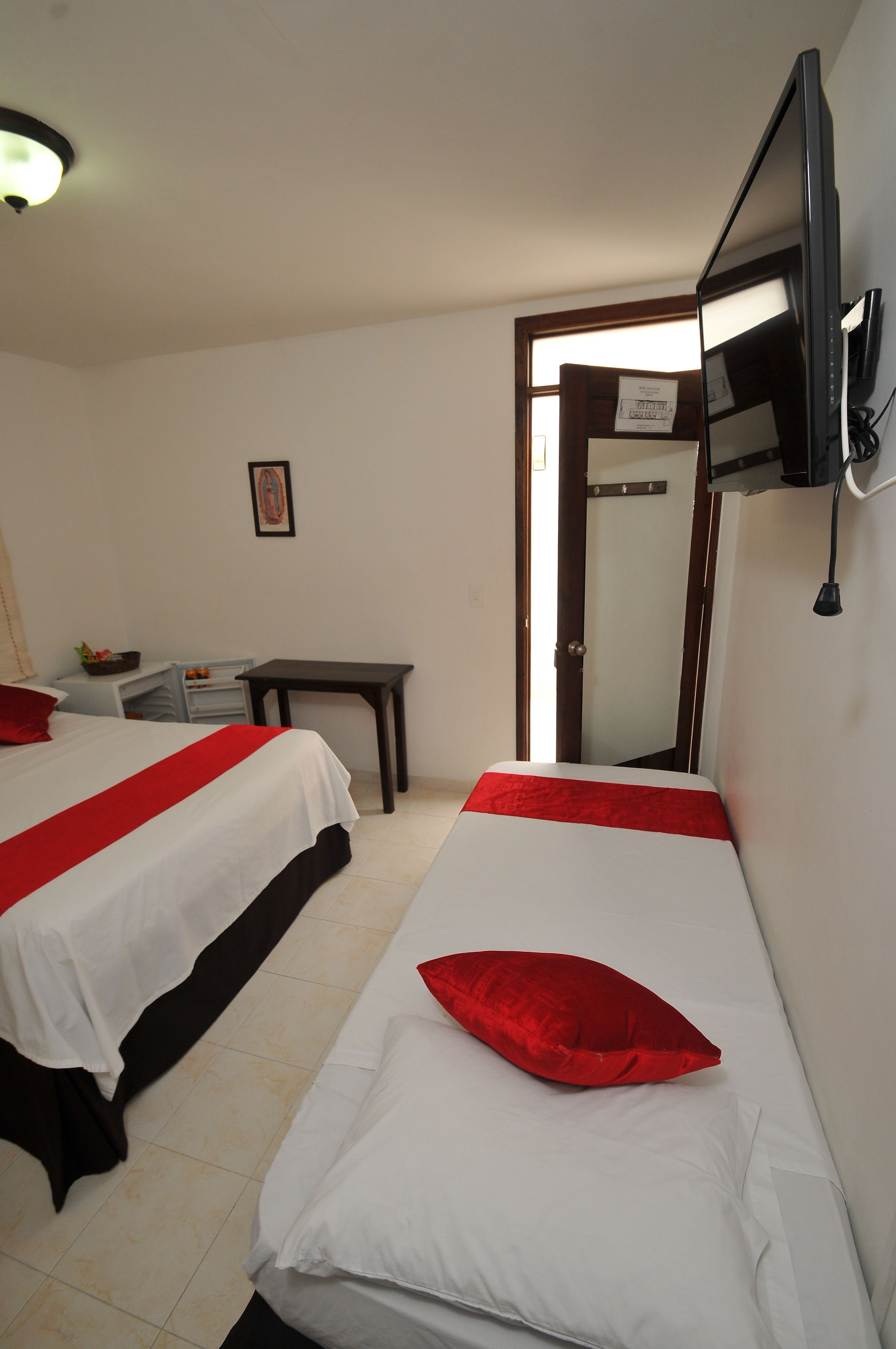 A hotel room with two beds, a desk, a chair, a TV mounted on the wall, and a door leading to another room.