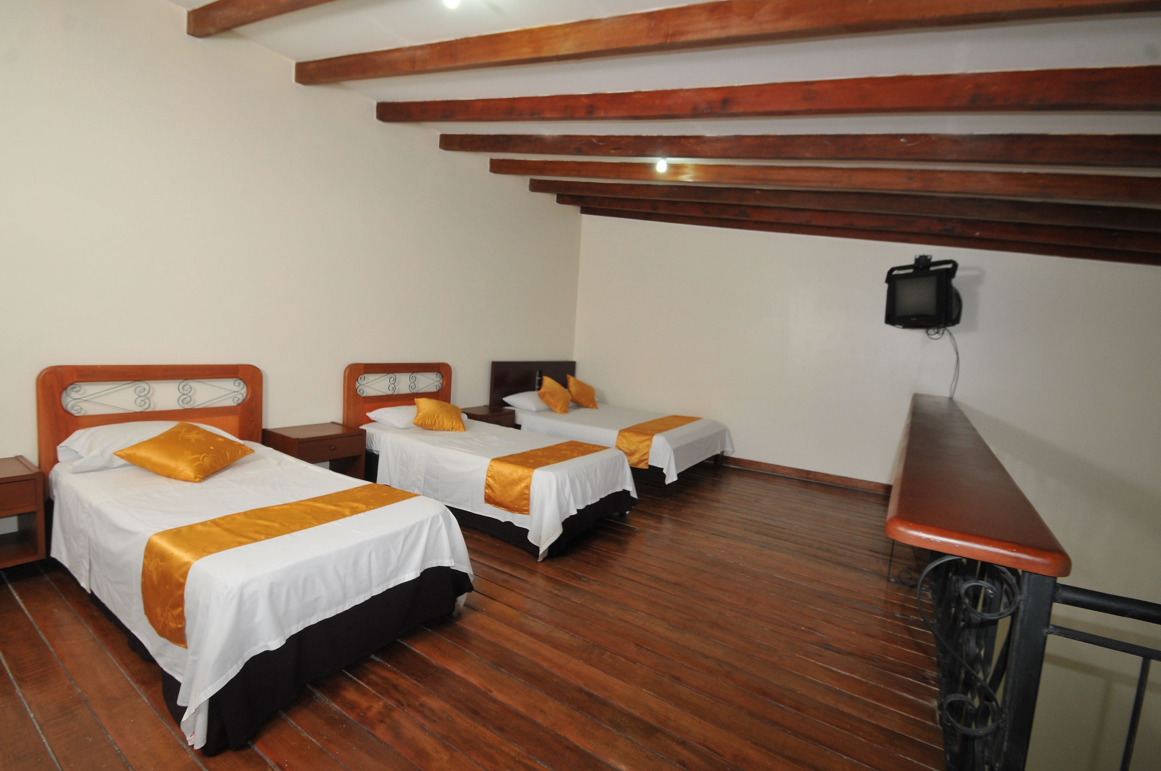 Habitación de hotel con tres camas individuales, piso de madera y techo de madera.