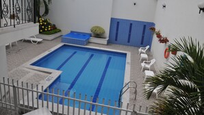 A swimming pool with a tiled deck, white lounge chairs, and potted plants. - Hotel San Julian (Guadalajara de Buga)