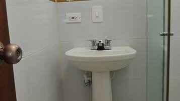 Un baño con lavamanos pedestal, cabina de ducha con mampara de vidrio y puerta de madera.
