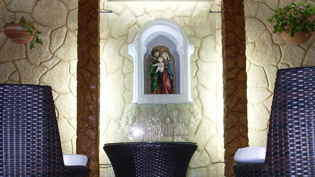 A stone wall with a religious statue, two wicker chairs, and a tiled floor. - Hotel San Julian (Guadalajara de Buga)