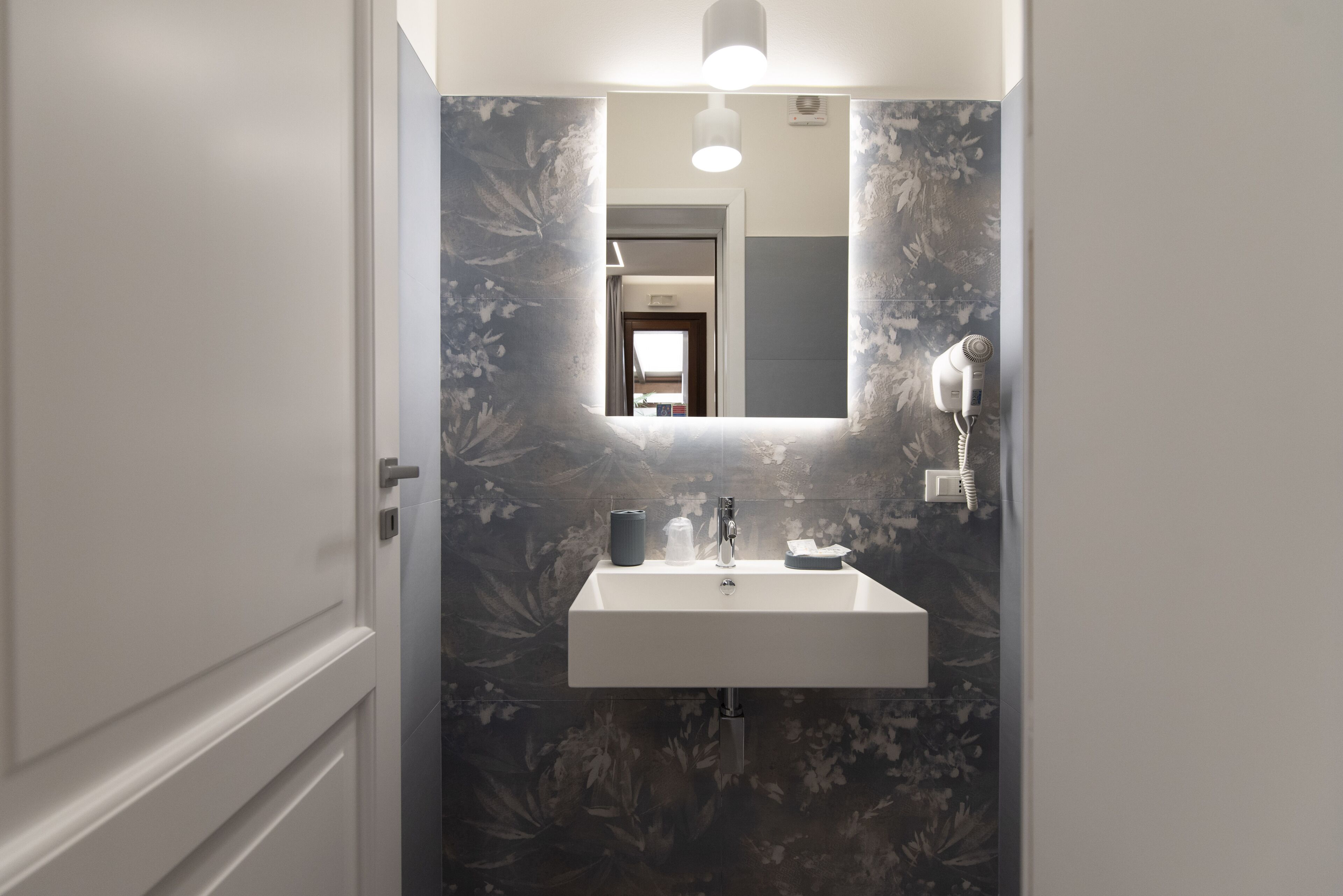 A bathroom with a white sink, a mirror above it, and a floral wallpaper design.