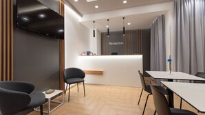 A modern reception area with a flat-screen TV, a reception desk, and a seating area with chairs and a table. - Room & Breakfast Aloe (San Vito Lo Capo)