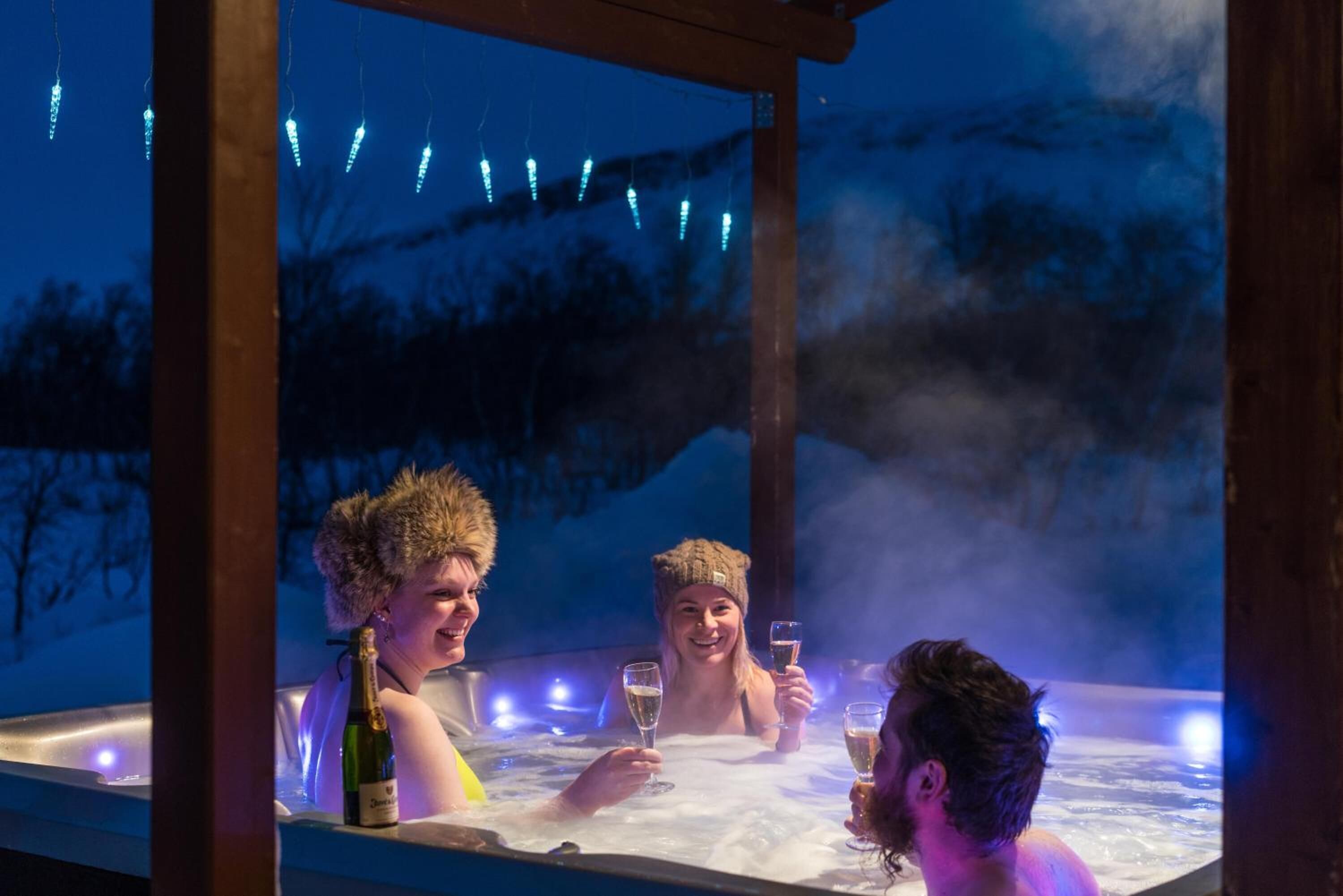 A hot tub with three people, surrounded by a wooden structure and string lights.