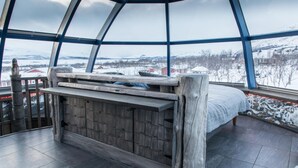 A cozy room with a wooden bed, a bench, and a view of snowy mountains and houses. - Tundrea (Enontekio)