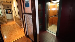 A hallway with a marble floor leading to an elevator.