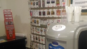 A hotel reception area with a wall displaying various travel brochures and a large water dispenser.