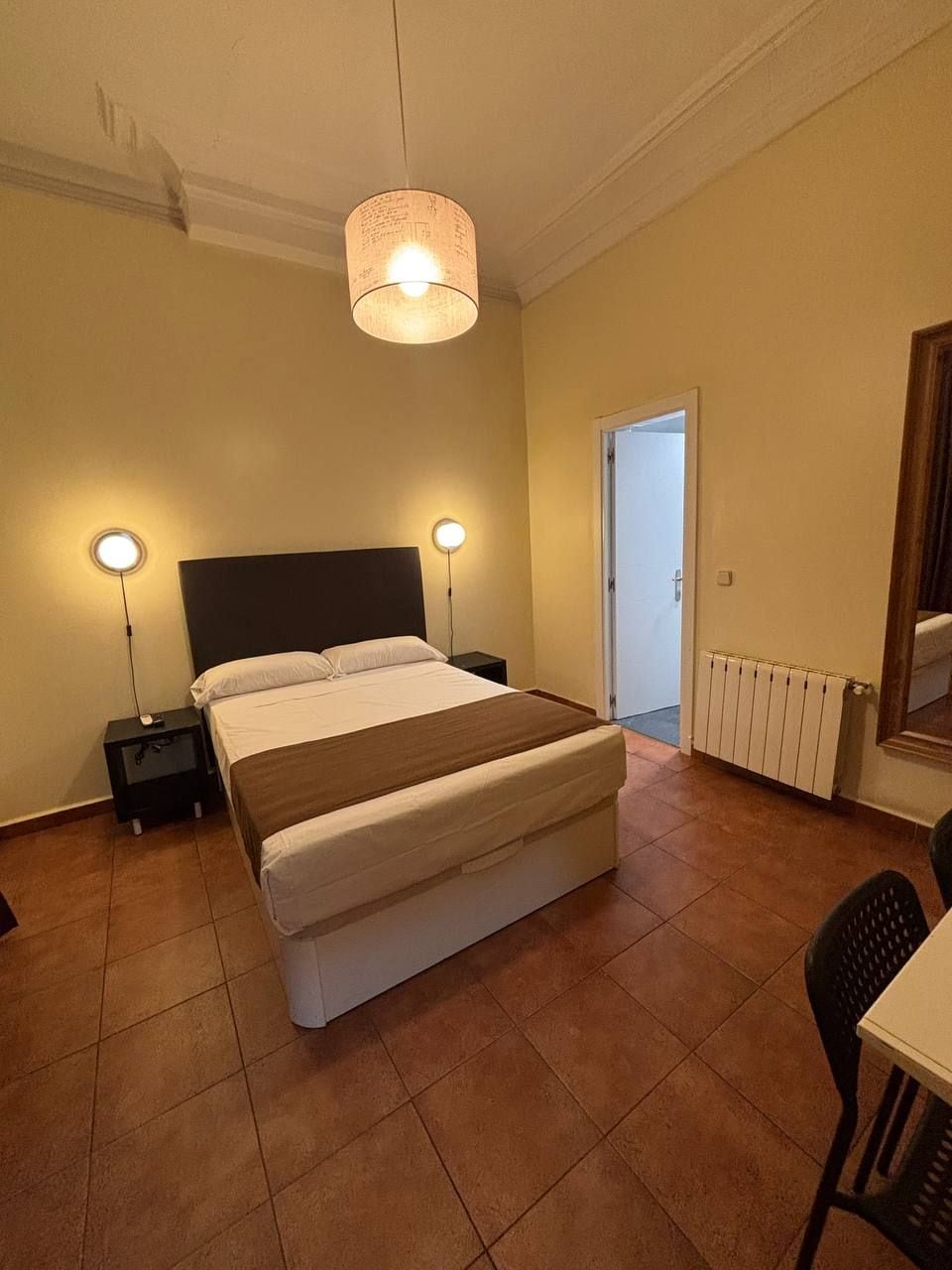 A bedroom with a bed, bedside lamps, a radiator, and a door leading to another room.