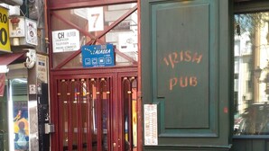 A pub entrance with a red door, a sign for 'CH OLIVER' above it, and a blue sign indicating 'EUROPA ALASKA' on the wall.