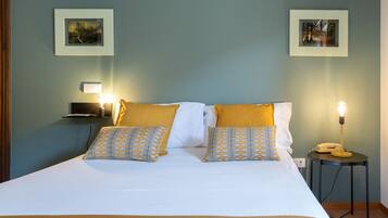 A neatly made bed with white and yellow bedding, two patterned pillows, a bedside lamp, and two framed pictures on the wall.
