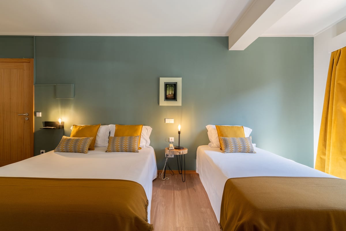 Une chambre d’hôtel avec deux lits, une table de chevet, un tableau encadré au mur et une fenêtre avec des rideaux.