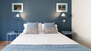 Une chambre à coucher avec un lit, deux tables de chevet, deux lampes et deux tableaux encadrés accrochés au mur.