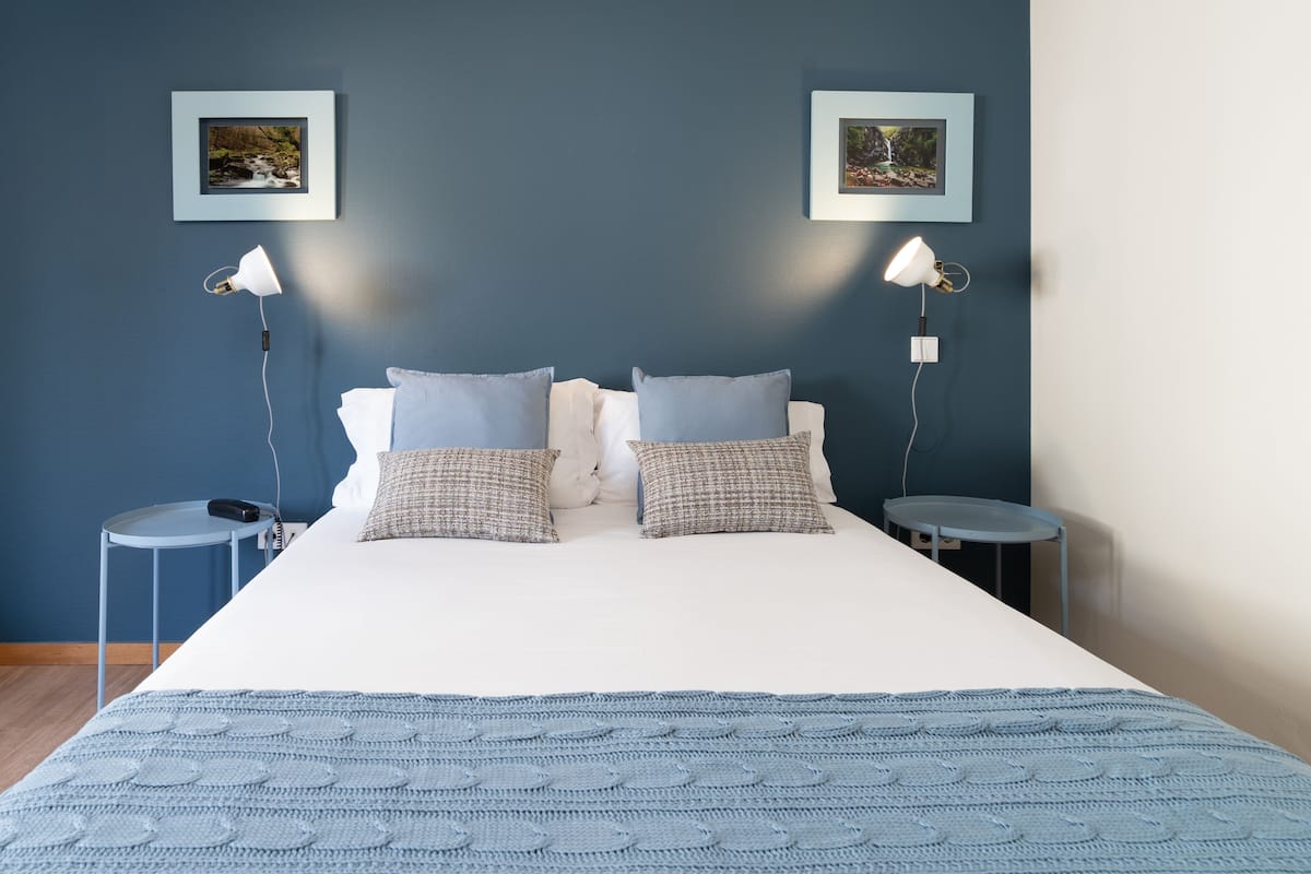 Une chambre à coucher avec un lit, deux tables de chevet, deux lampes et deux tableaux encadrés accrochés au mur.