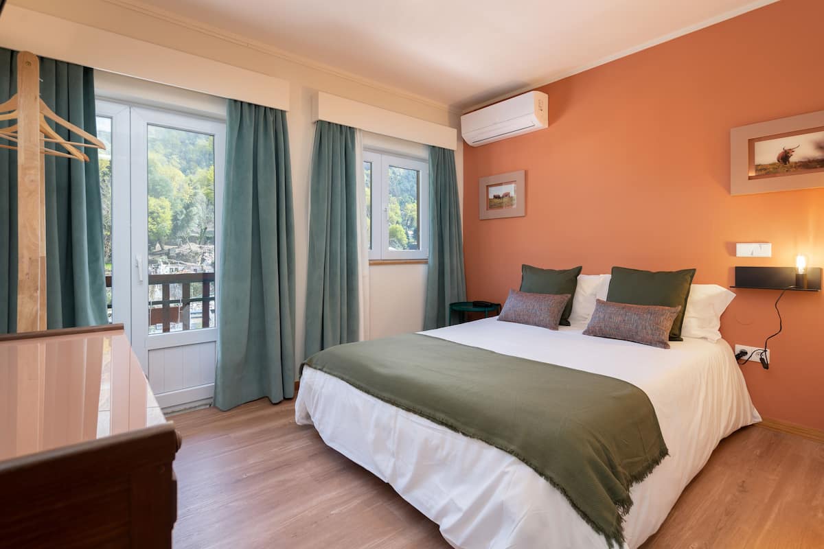 Une chambre à coucher avec un grand lit, une commode en bois, un bureau et une fenêtre avec des rideaux.