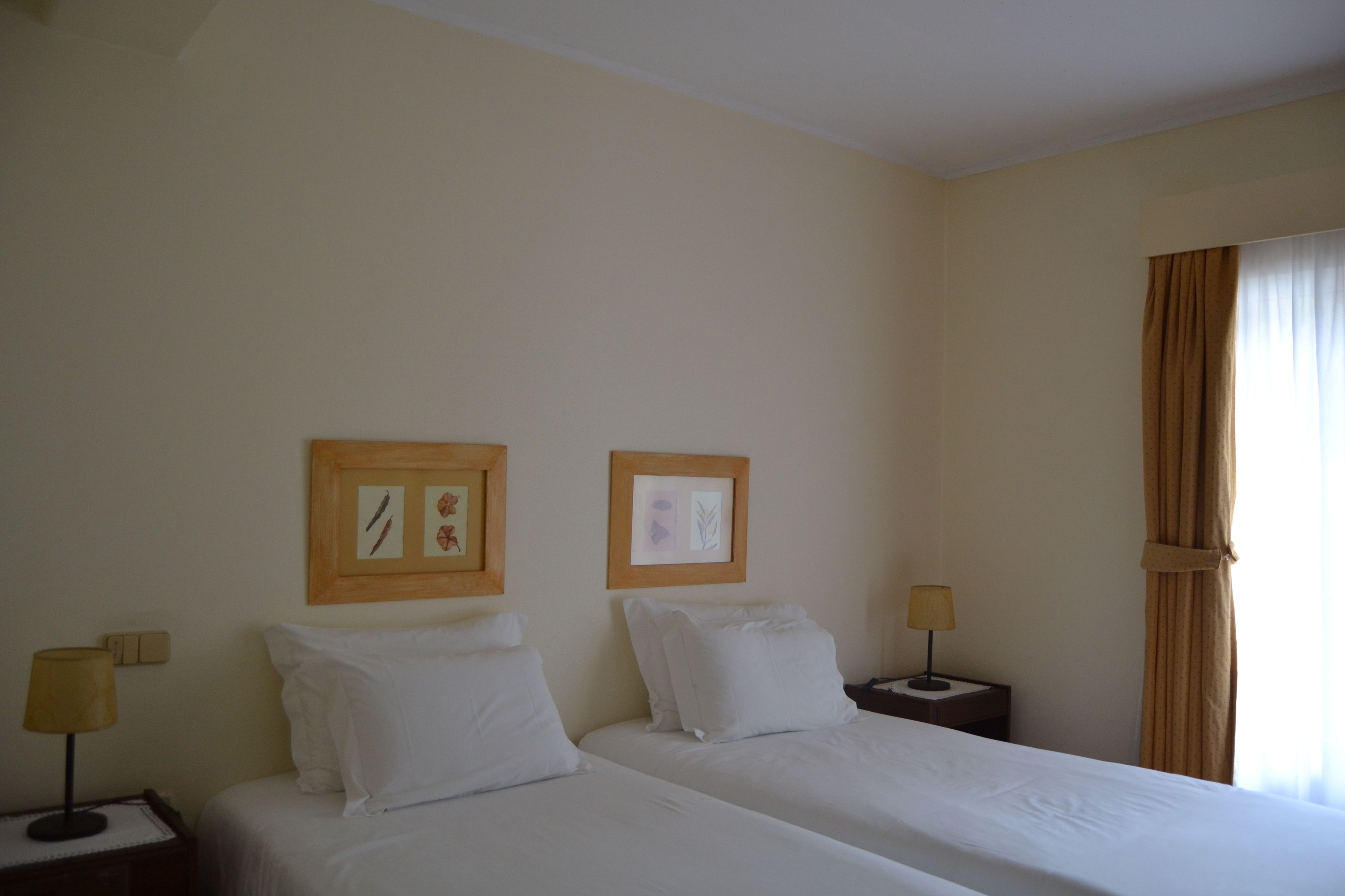 Una camera d'albergo con due letti singoli, un comodino con una lampada e quadri appesi al muro.
