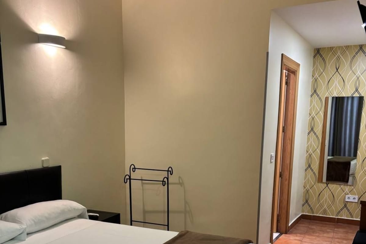 A bedroom with a bed, bedside table, and a wall-mounted light fixture.