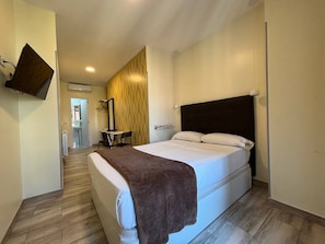 A hotel room with a bed, a flat-screen TV mounted on the wall, a small table with a chair, and a wooden floor. - Hostal Alaska (Madrid)