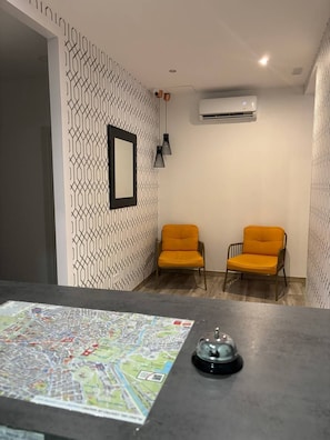 A room with two yellow chairs, a black table with a map, a bell, and an air conditioning unit. - Hostal Alaska (Madrid)