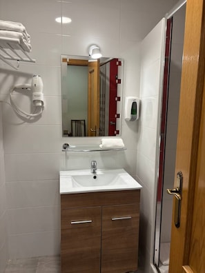 A bathroom with a white sink, a mirror, a towel rack, a hand dryer, and a glass shower enclosure. - Hostal Alaska (Madrid)