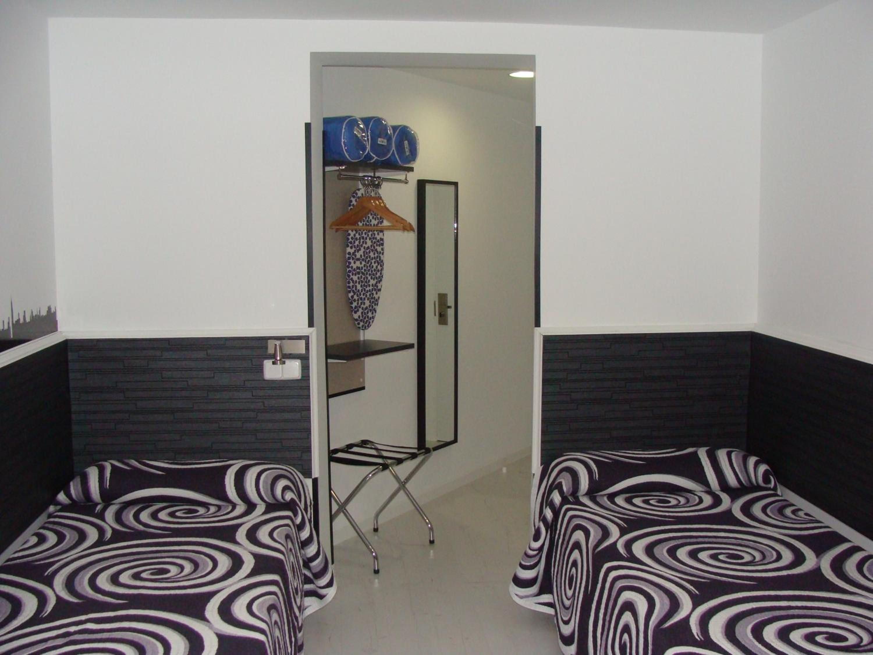 Habitación de hotel con dos camas individuales, un armario, un espejo y un pequeño estante.