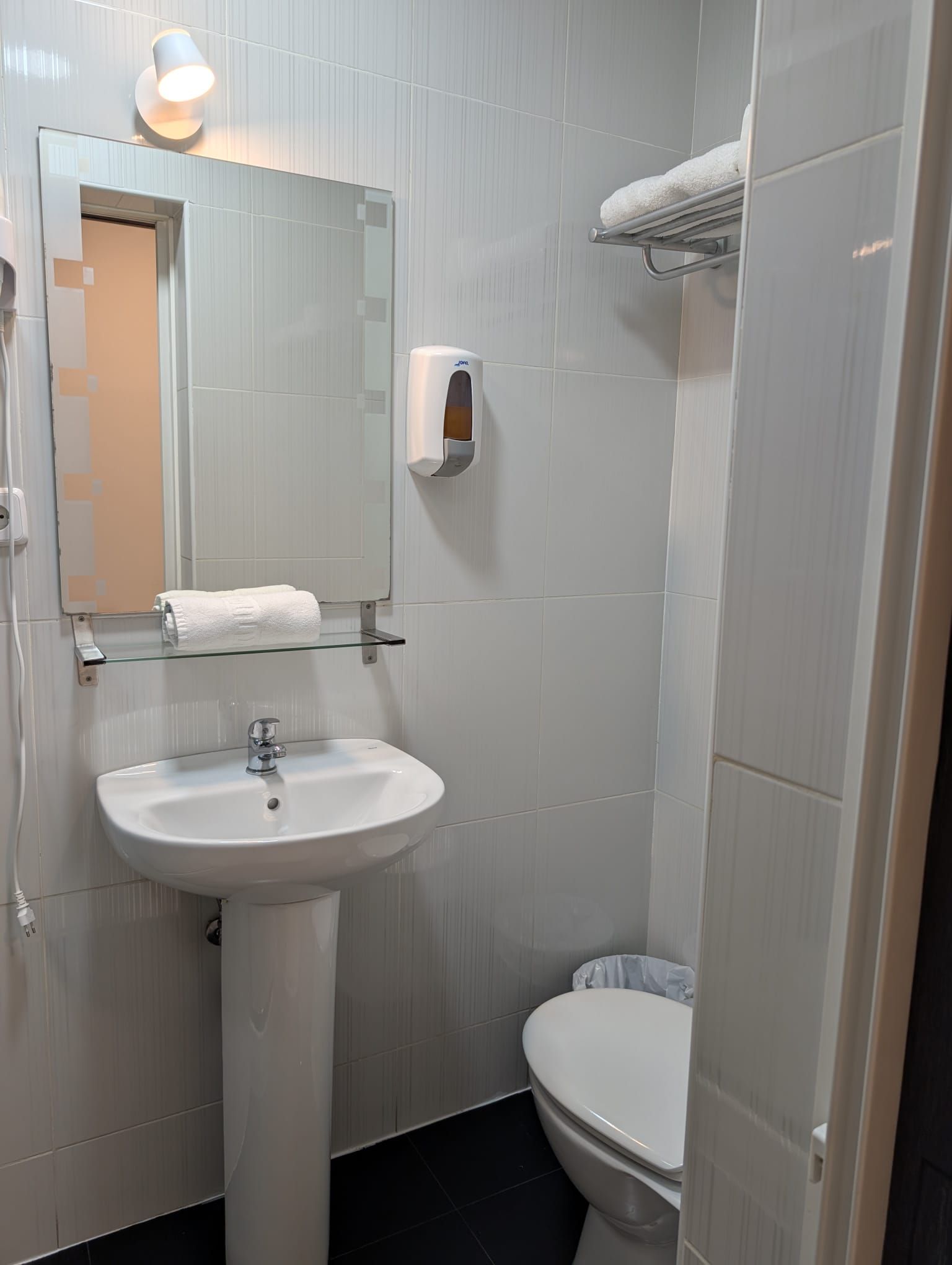 Un baño con lavamanos blanco, espejo, inodoro y toallero.