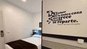 Un dormitorio pequeño y moderno con cama, mesita de noche y una pared con una cita decorativa.