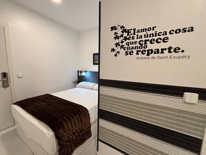 A small, modern bedroom with a bed, a bedside table, and a wall with a decorative quote. - Hostal JQ Madrid 1 (Madrid)
