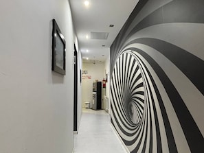 A hallway with a black and white striped wall design, a framed picture on the left, and a vending machine in the distance. - Hostal JQ Madrid 1 (Madrid)