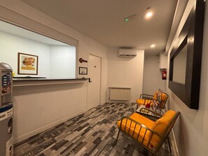 A room with a patterned floor, a sofa with yellow cushions, a small table, a window with artwork, and a wall-mounted air conditioning unit. - Hostal JQ Madrid 1 (Madrid)