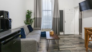 A modern living room with a grey sofa, a coffee machine, a wooden table, and a TV mounted on the wall. - BeiRoom Hyde Park Apartments (London)