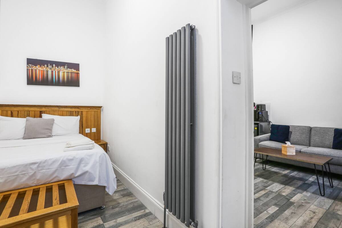 Een hotelkamer met een bed, een houten bankje, een radiator, een sofa en een schilderij aan de muur.
