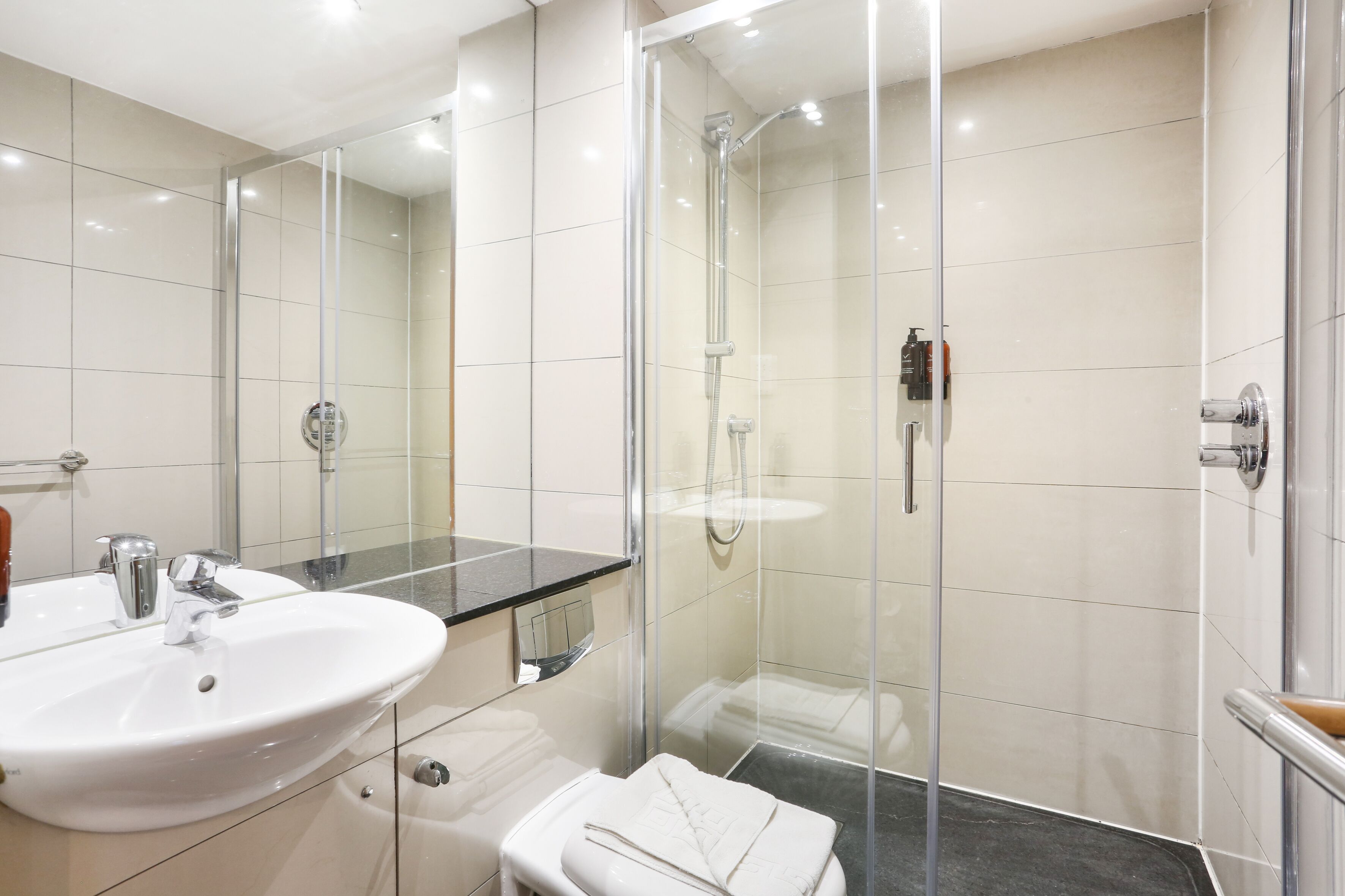 A modern bathroom with a glass-enclosed shower, a white sink, and a large mirror.