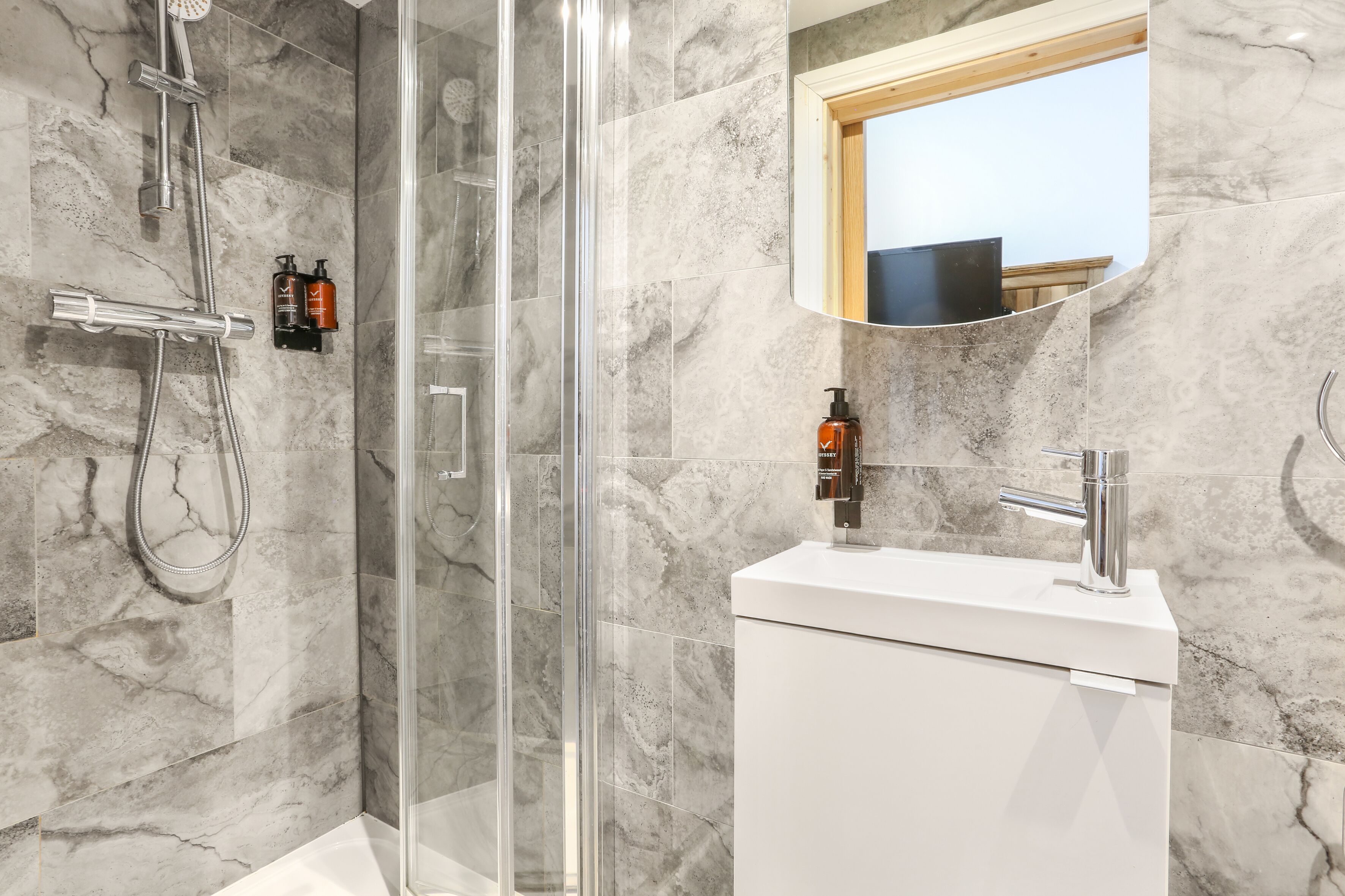 Ein modernes Badezimmer mit einer gläsernen Duschkabine, einem weißen Waschbecken und Marmorwänden.