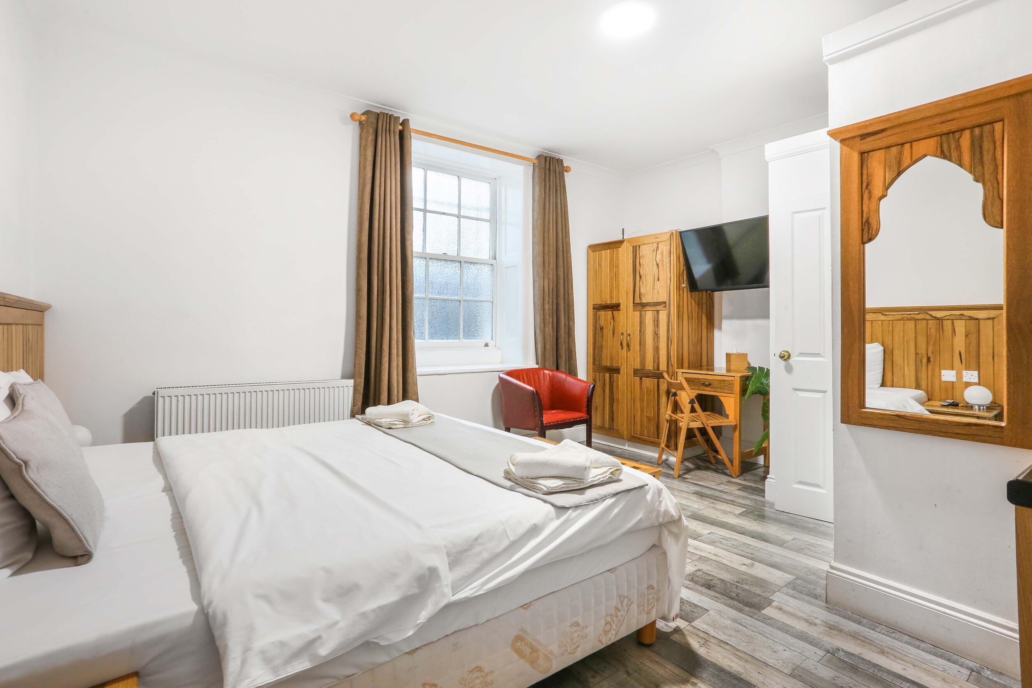 A hotel room with a bed, a desk, a chair, a TV, and a wardrobe.