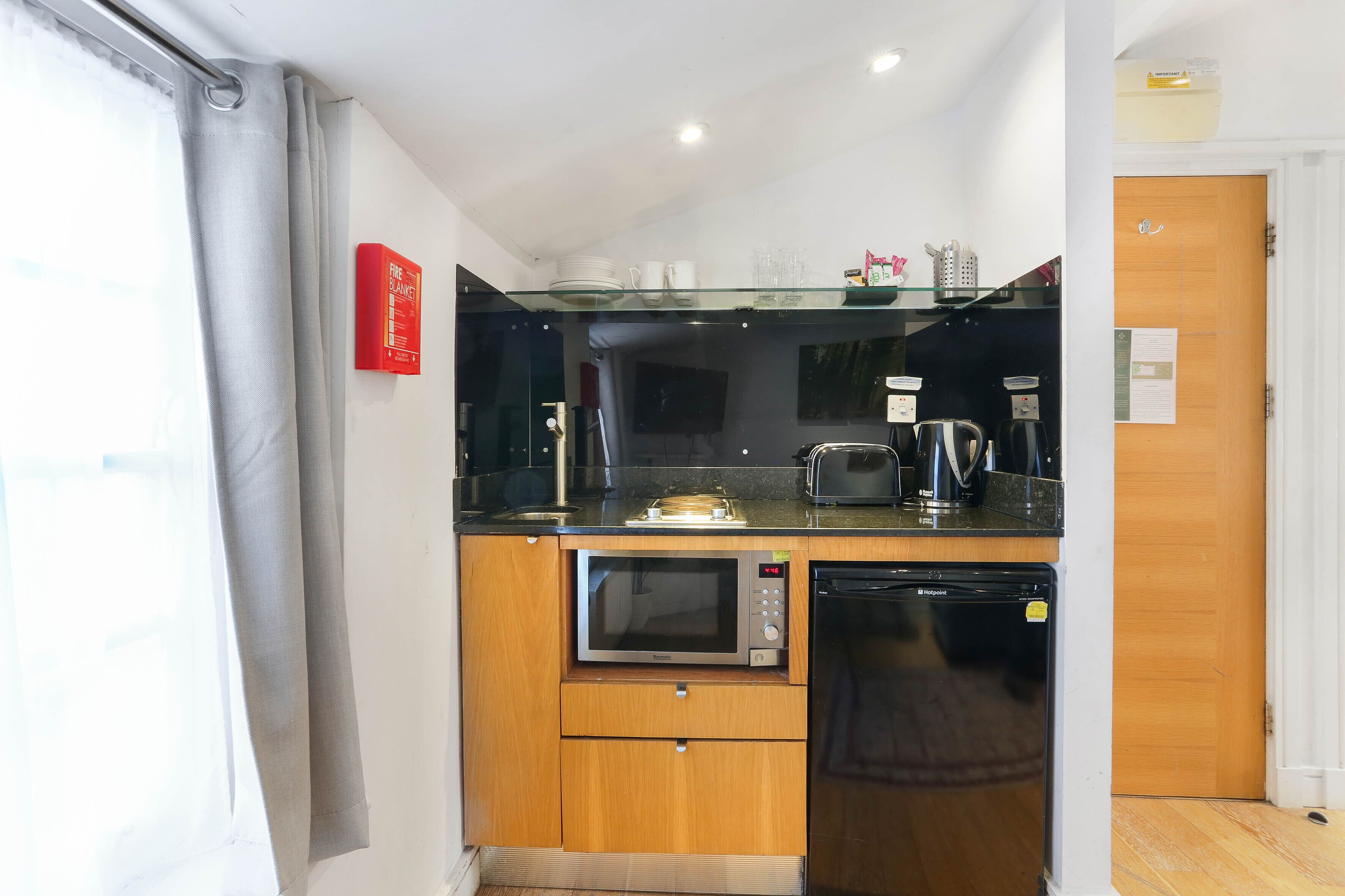 Cocina compacta con microondas, tostadora y cafetera sobre una encimera de vidrio.