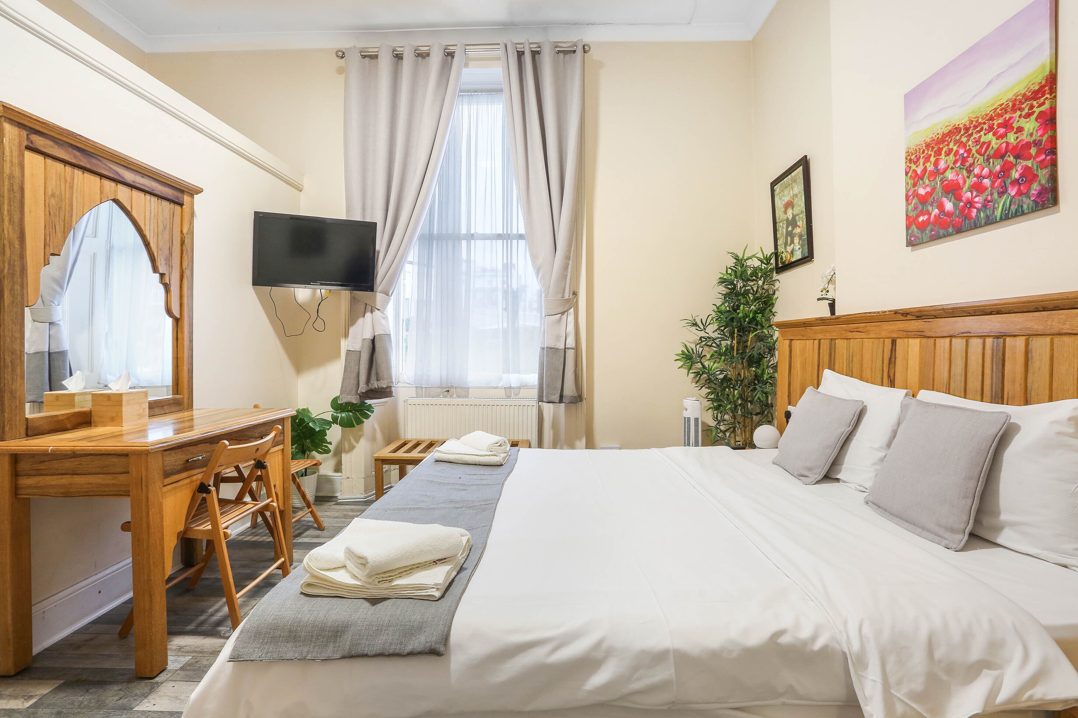 A hotel room with a bed, a desk, a chair, a TV, and a window with curtains.