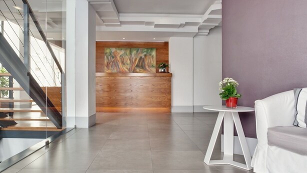 A modern lobby with a staircase, a reception desk with a painting, and a seating area with a plant. - Rossio Hotel (Portalegre)