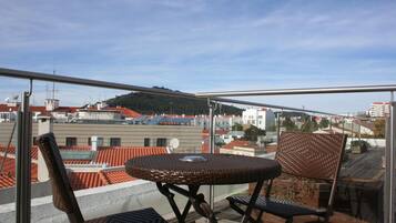 A balcony with wicker furniture, a table, and a view of buildings and a hill.